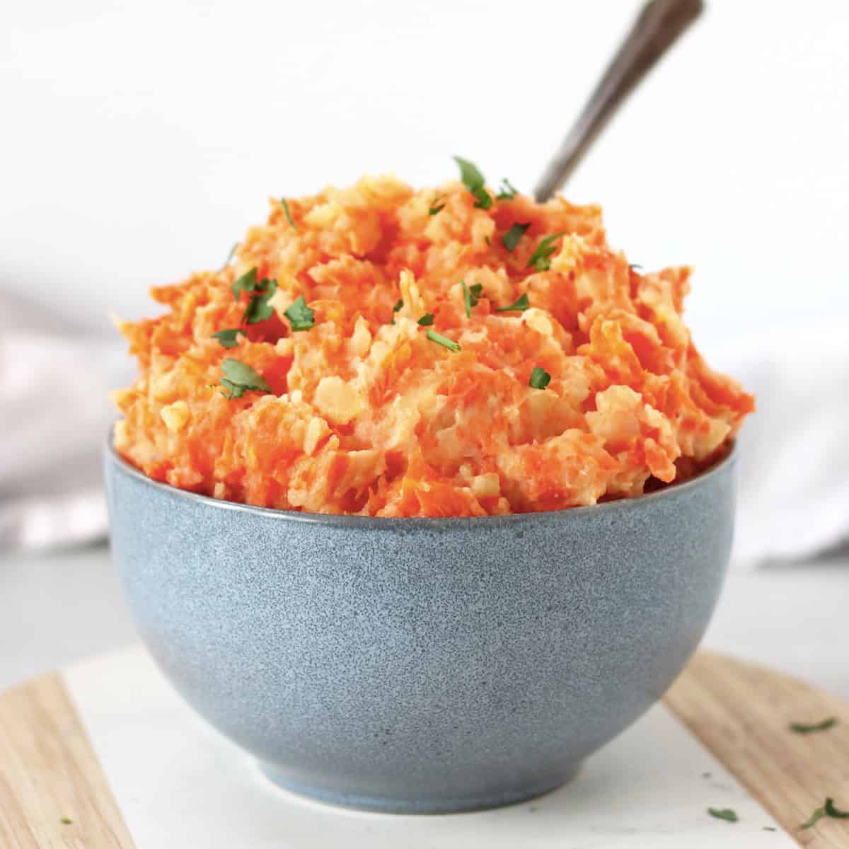 Carrot and potato mash in a blue bowl with a serving spoon.