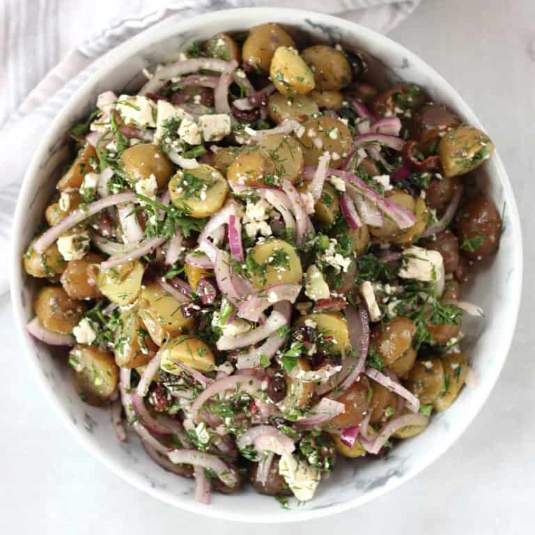 Greek potato salad with feta, olives, onions and fresh herbs in a white bowl.