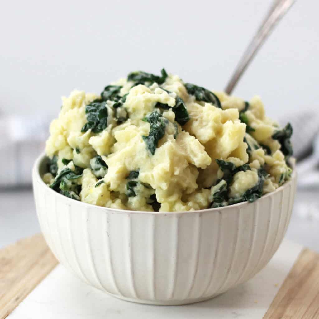 A bowl of spinach mashed potato with a serving poon.