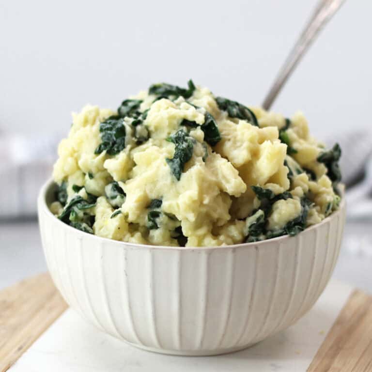 A bowl of spinach mashed potato with a serving poon.