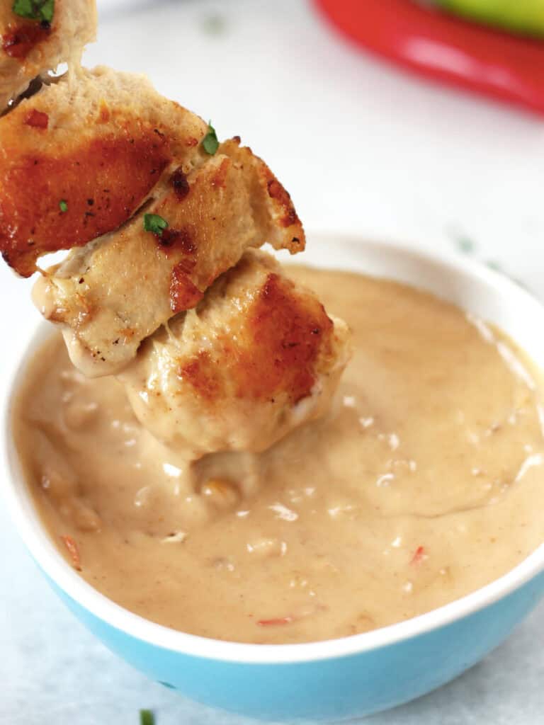 Chicken being dipped in peanut sauce.