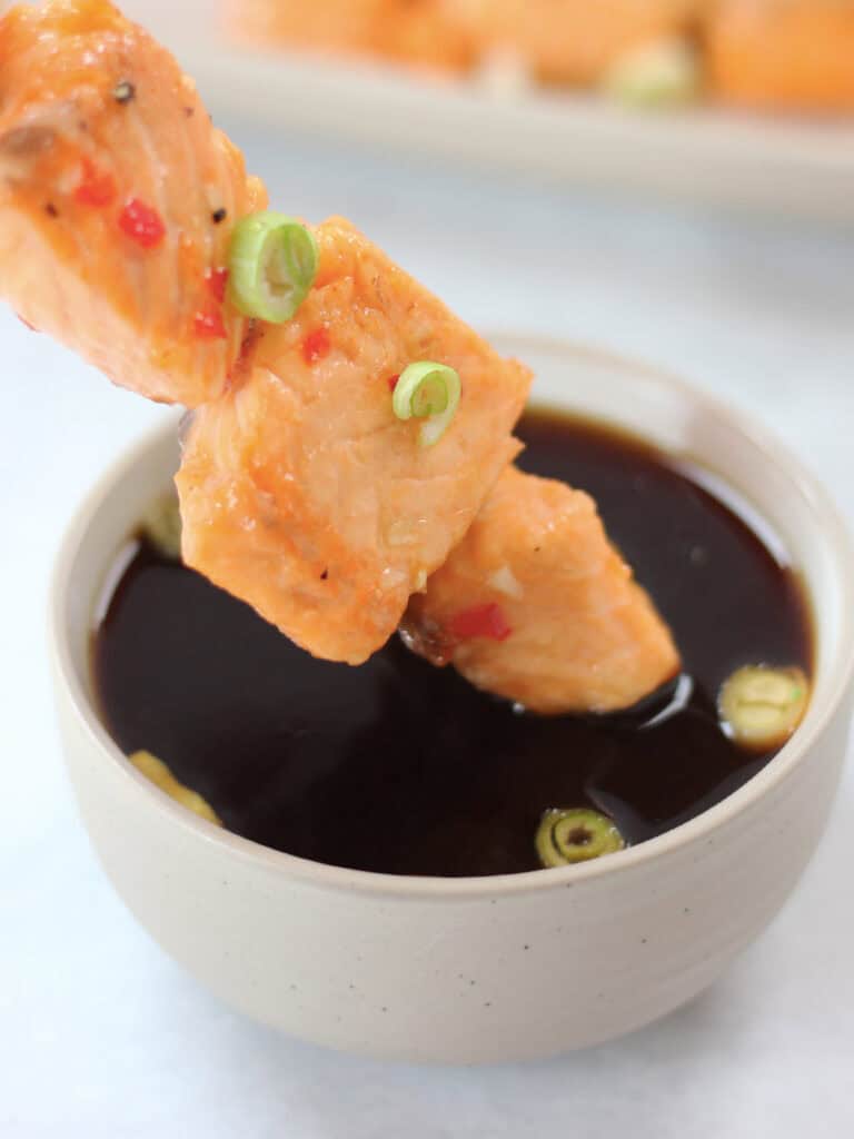 A salmon skewer being dipped in sauce.