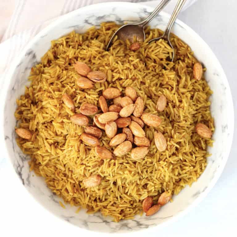 Two spoons in a bowl of Egyptian rice topped with fried almonds.