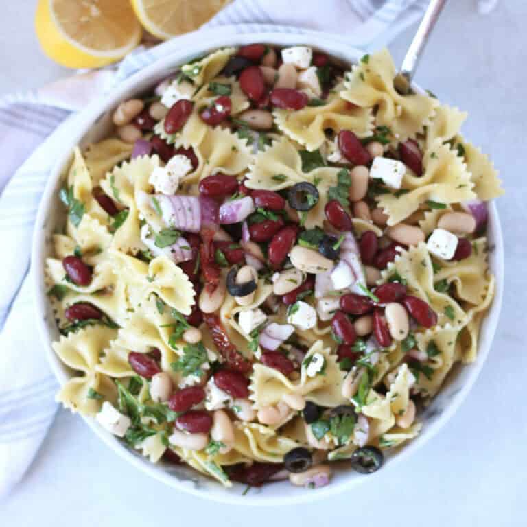 A large serving bowl with pasta salad with beans, feta, red onion and olives.
