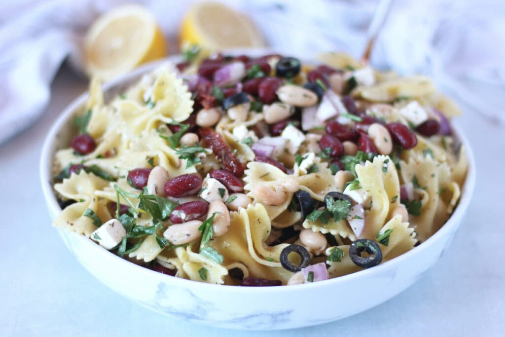 Bowtie pasta salad with herbs, beans and olives served in a bowl.