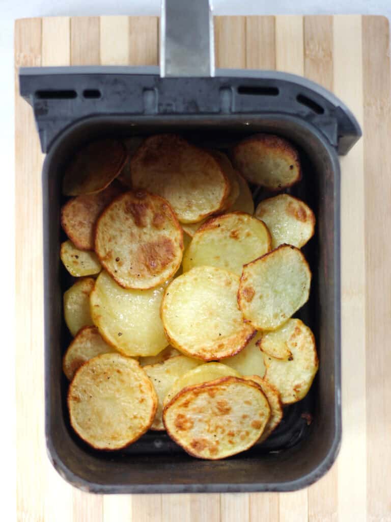 Cooked potato slices in an air fryer basket.