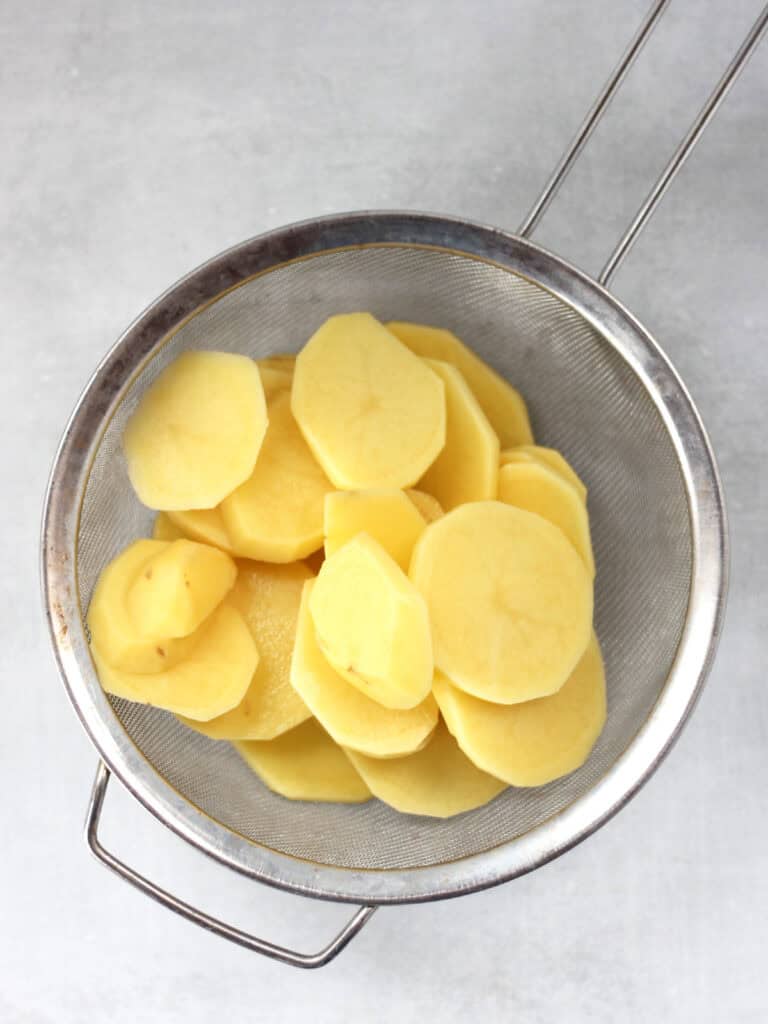 Sliced potatoes in a fine mesh sieve.