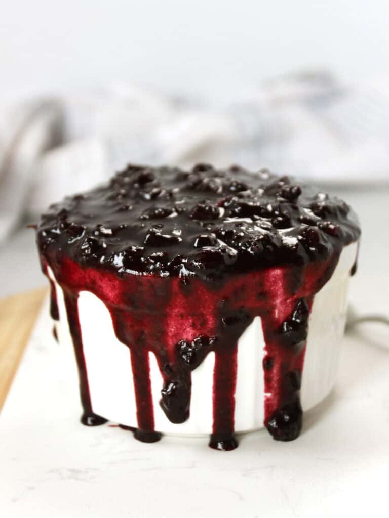 Blueberry sauce overflowing in a white ramekin.