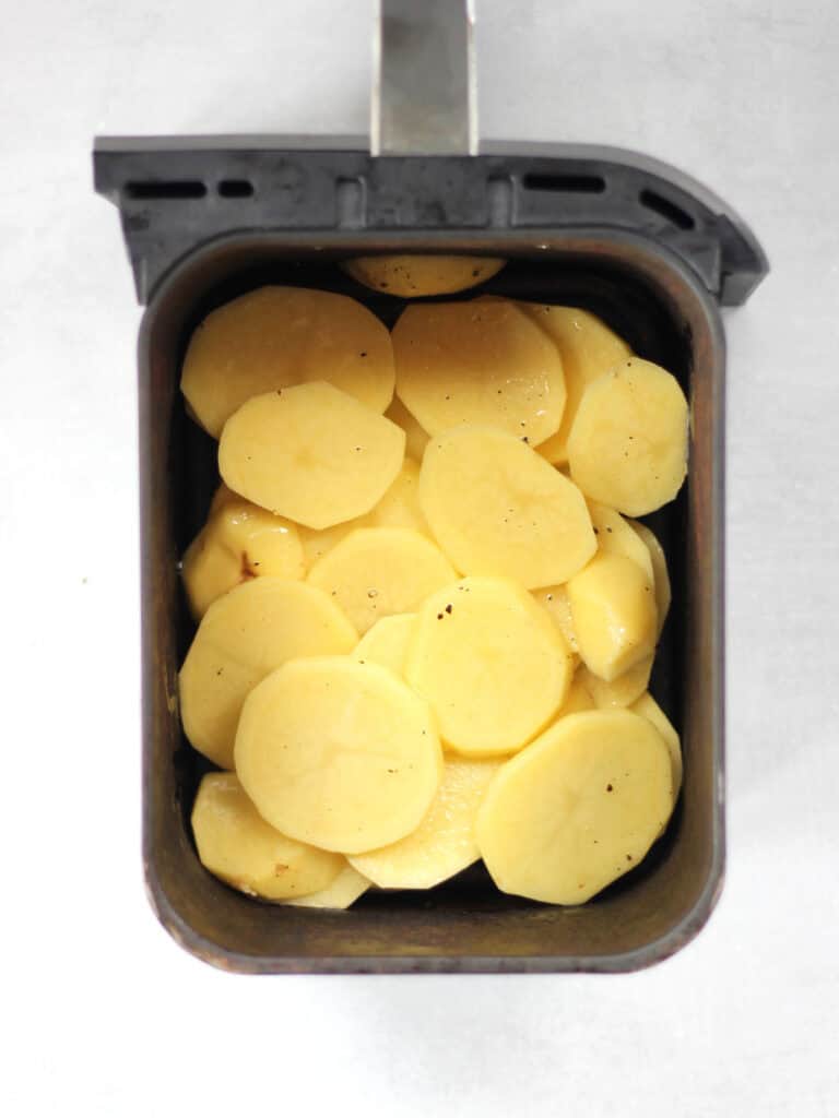 Uncooked potatoes in an air fryer basket.