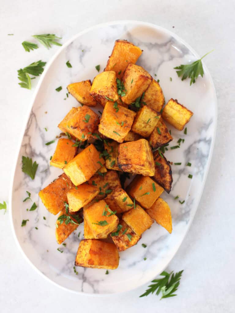 Butternut squash side dish served on a white plate with parsley garnish.