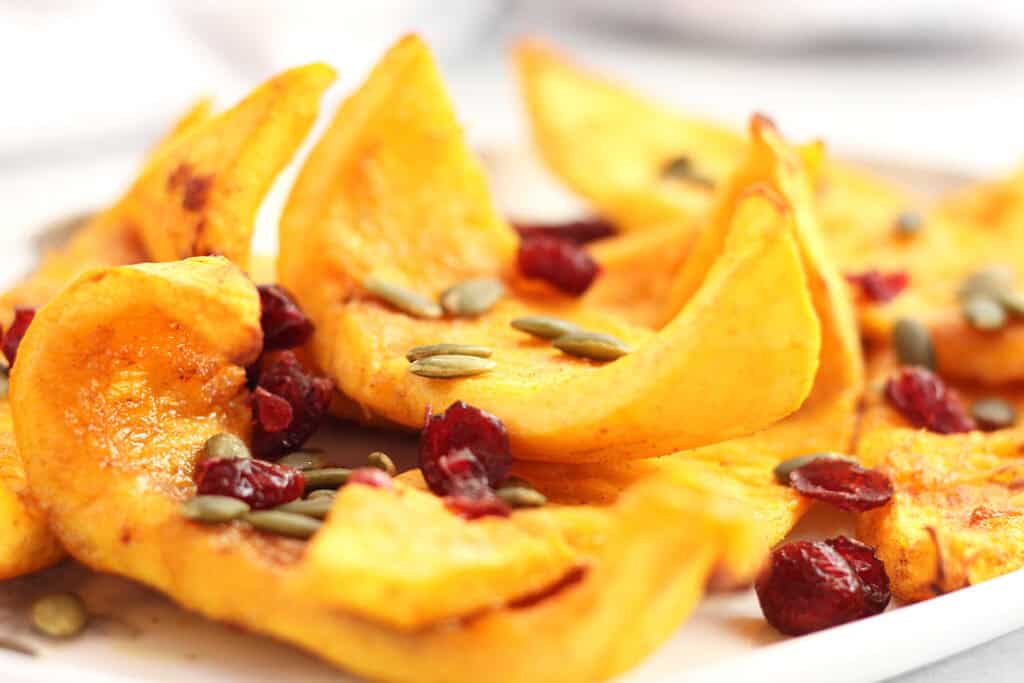 Wedges of roasted pumpkin garnished with pumpkin seeds and cranberries.