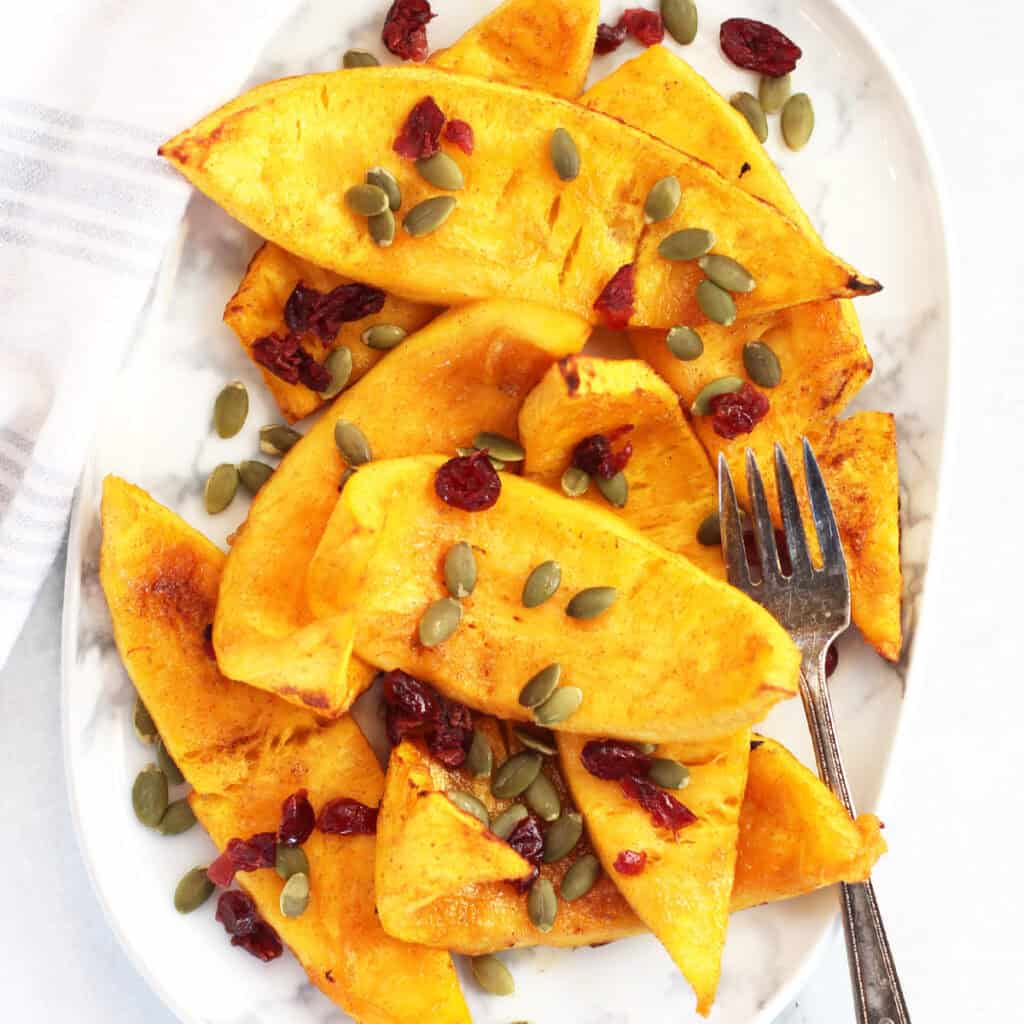 Air fried pumpkin wedges served on a plate with a garnish of pumpkin seeds and cranberries.