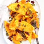 Air fried pumpkin wedges served on a plate with a garnish of pumpkin seeds and cranberries.