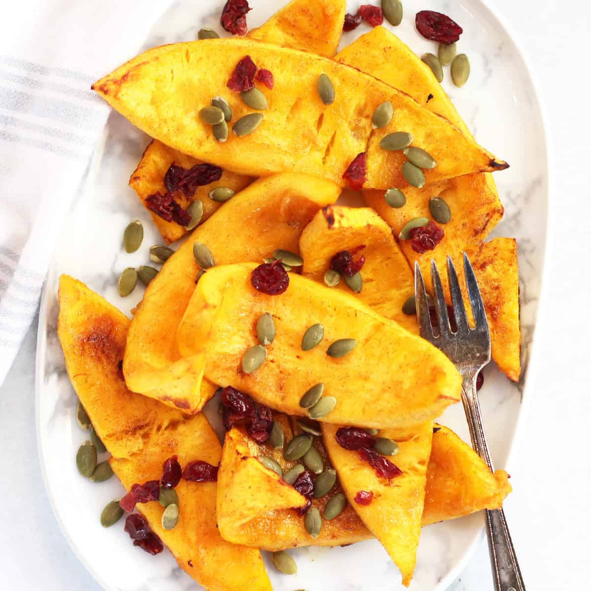 Air fried pumpkin wedges served on a plate with a garnish of pumpkin seeds and cranberries.
