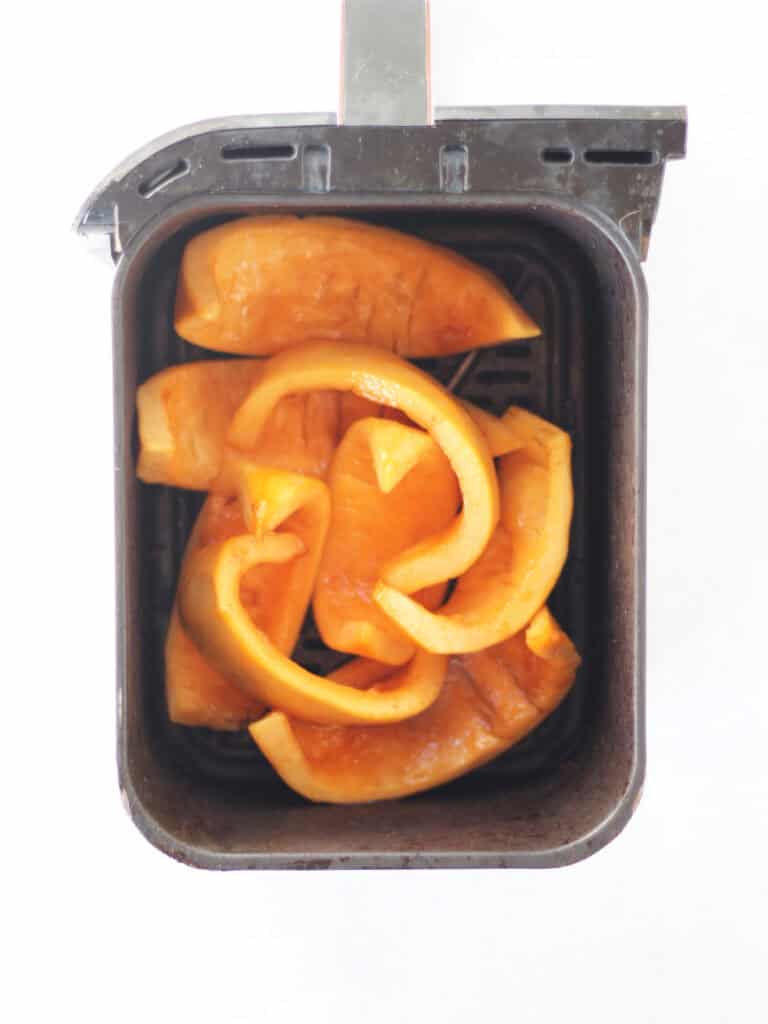 Seasoned uncooked pumpkin in an air fryer basket.