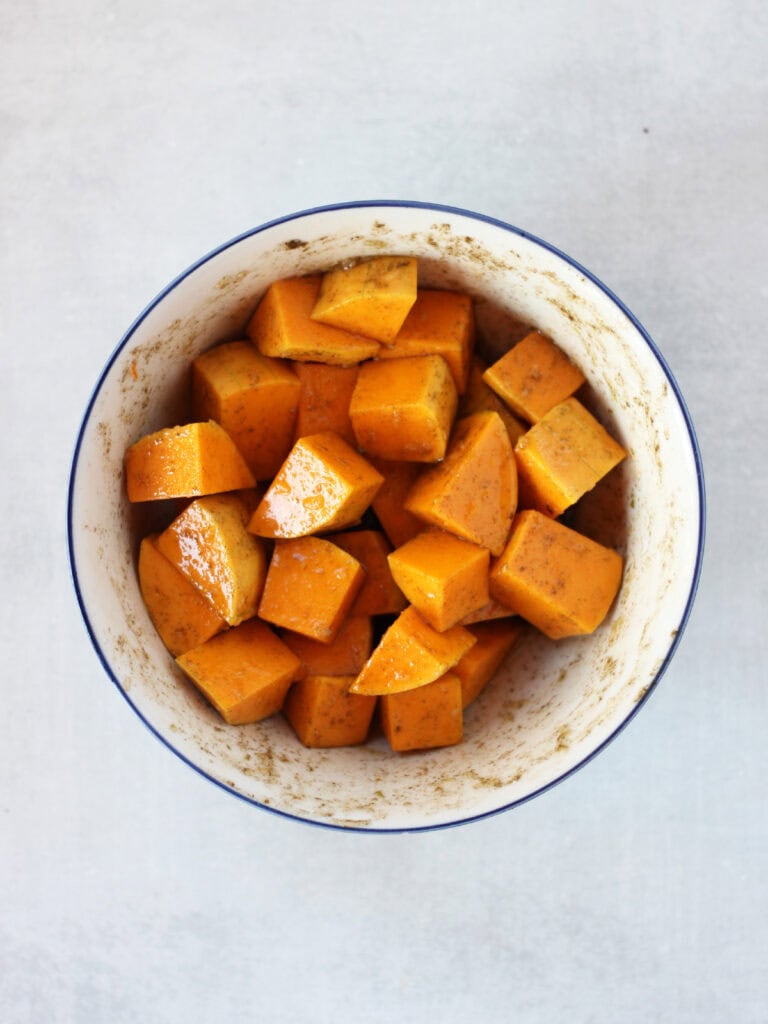 Butternut squash cubes tossed in seasoning in a bowl.