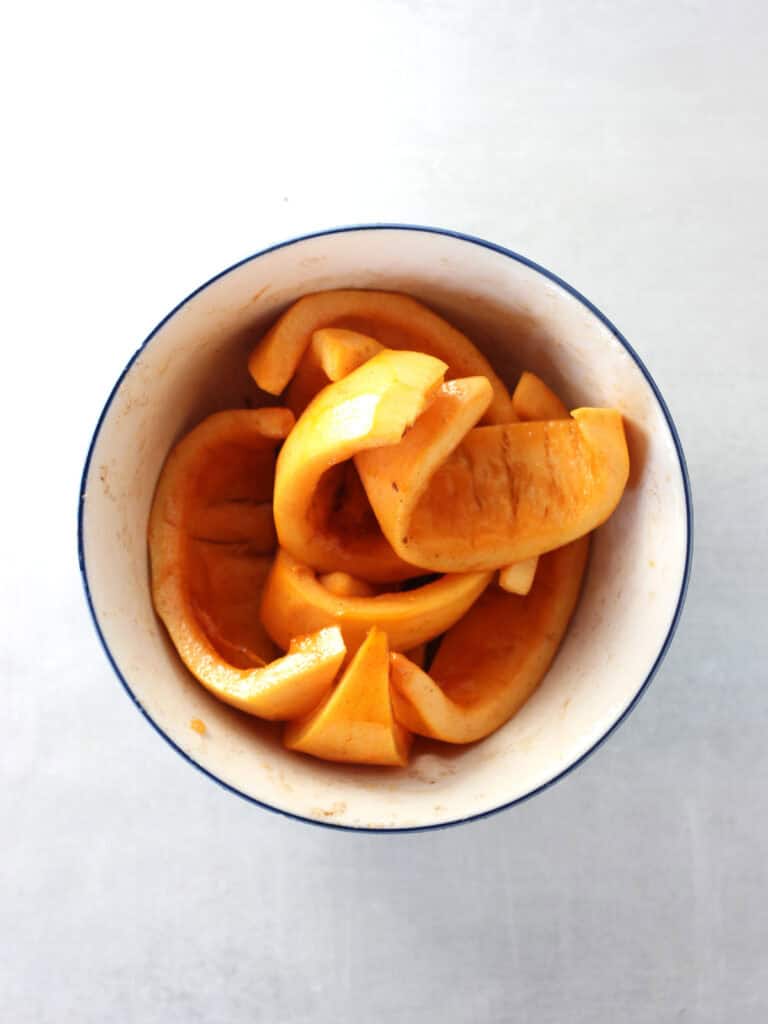Pumpkin wedges mixed with seasonings in a bowl.