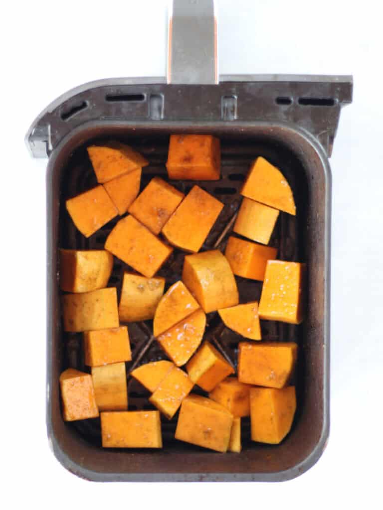 Uncooked butternut squash cubes in an air fryer basket.
