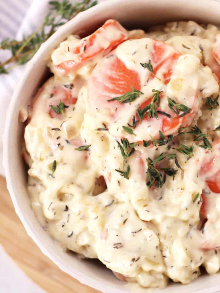 Sliced carrots in a cream sauce served in a bowl and garnished with fresh thyme.