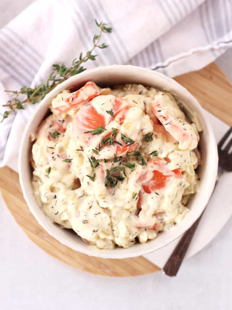 A bowl of creamed carrots next to a sprig of thyme.
