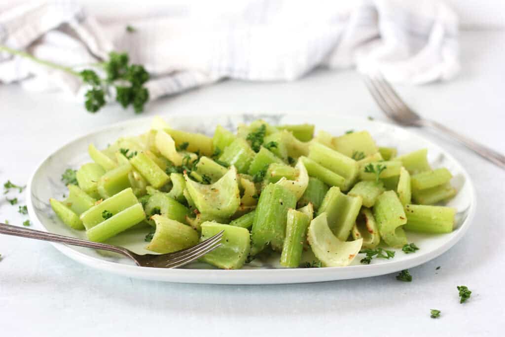 Cooked celery on a plate with fresh parsley garnish.