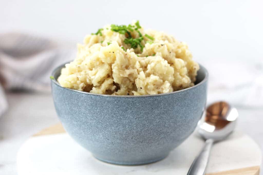 A bowl of mashed potatoes in a bowl next to a spoon.