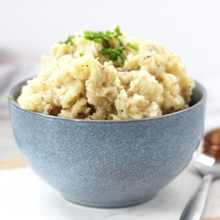 Black pepper mashed potatoes in a blue bowl with chive garnish.