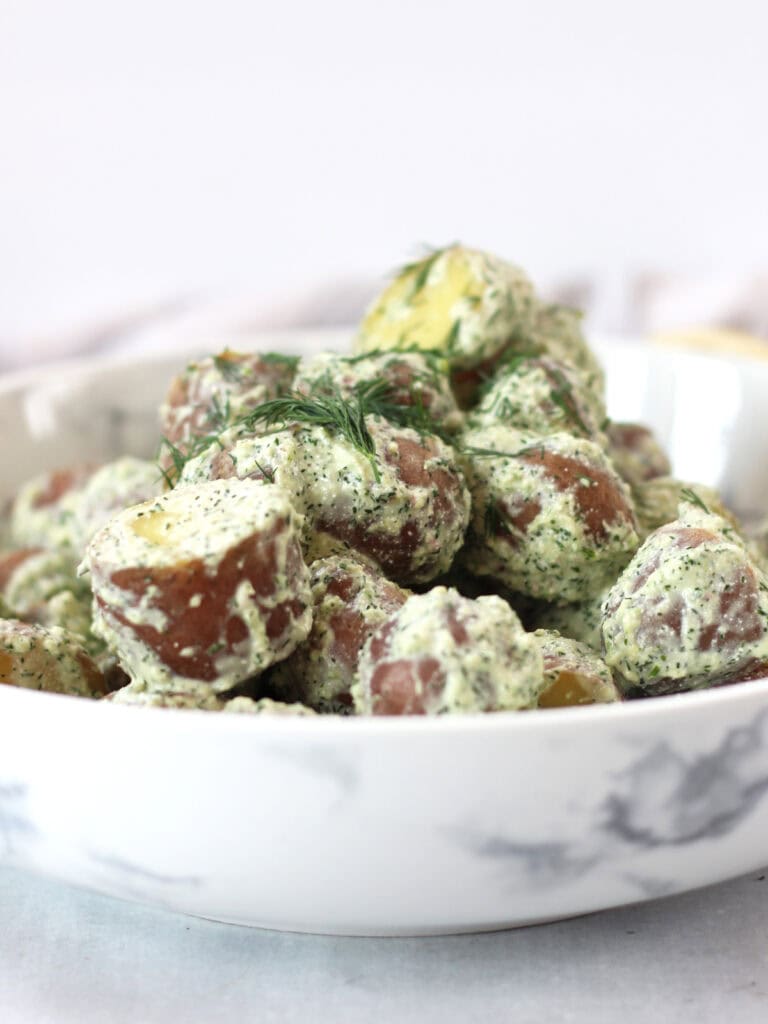 Red potato salad tossed in a creamy herb dressing served in a bowl.