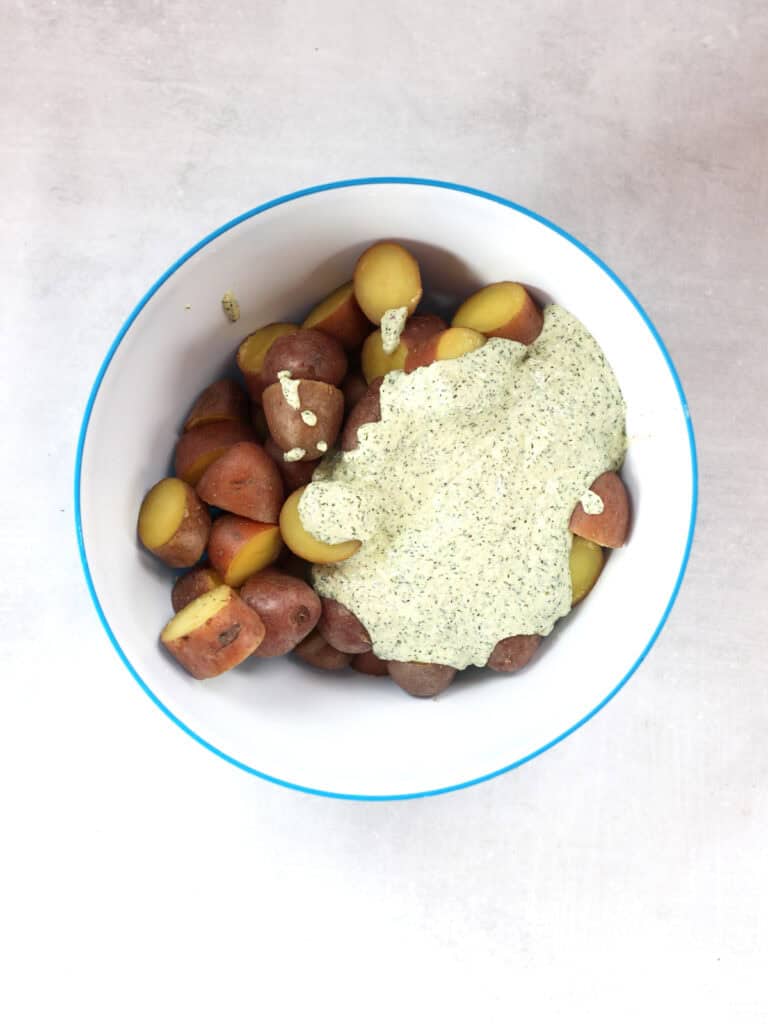 Dressing poured over cooked potatoes in a large mixing bowl.