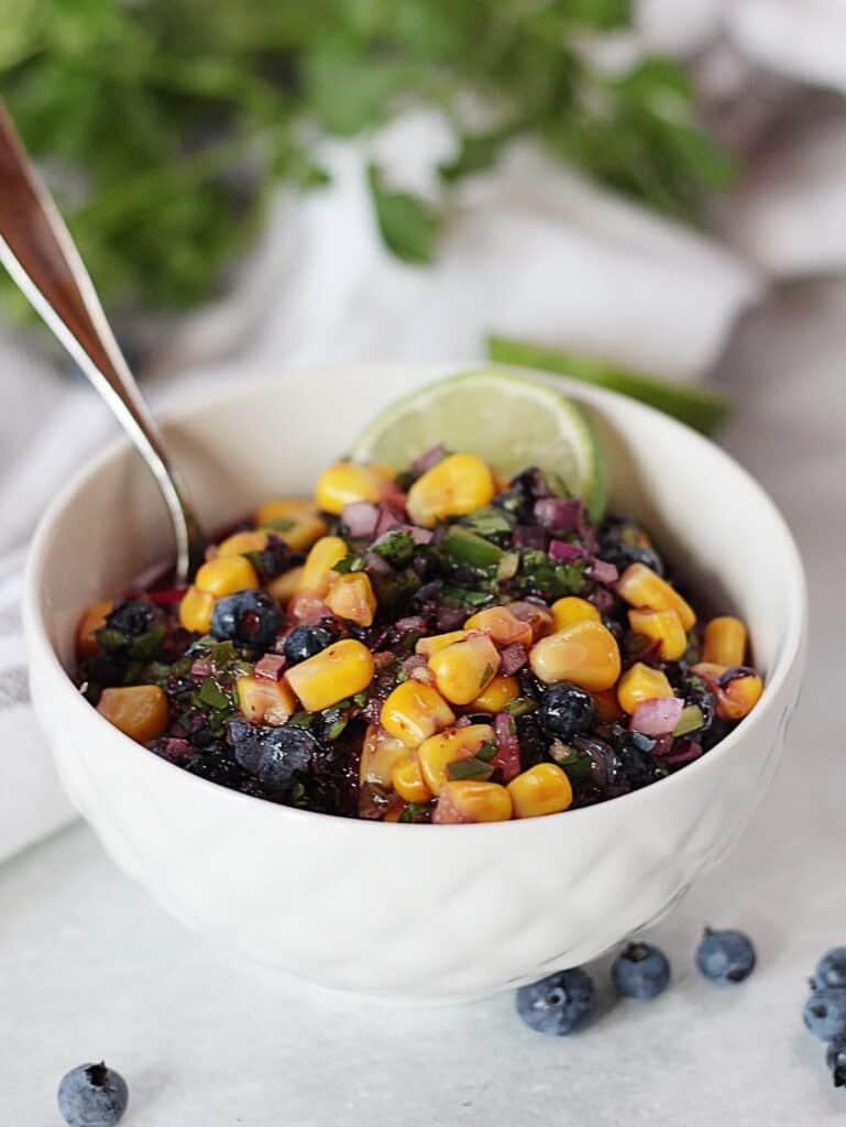 A spoon in a small bowl of blueberry salsa.