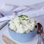 Mashed potato in a bowl next to two serving spoons.