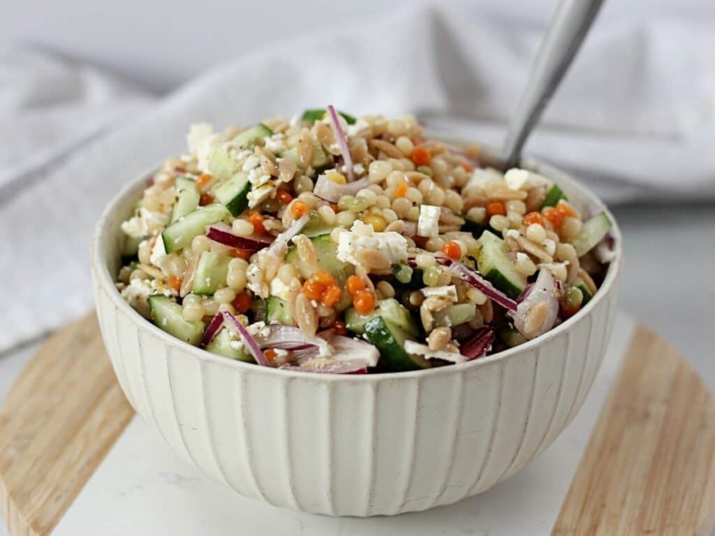 Israeli couscous salad served in a white bowl with a spoon.