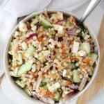 Pearl couscous with feta, cucumber and red onion in a serving bowl with a spoon.