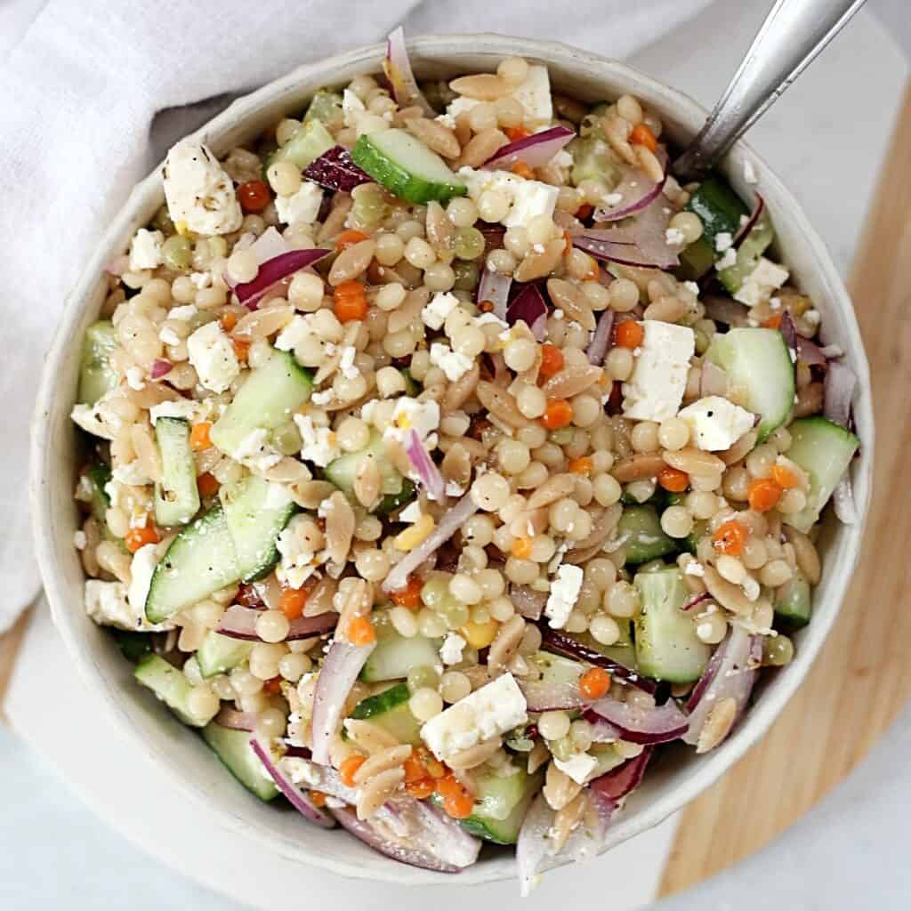 Pearl couscous side salad in a white bowl with a spoon.