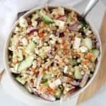 Pearl couscous side salad in a white bowl with a spoon.