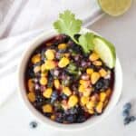 Blueberry and corn salsa in a white bowl garnished with a fresh lime slice and cilantro.