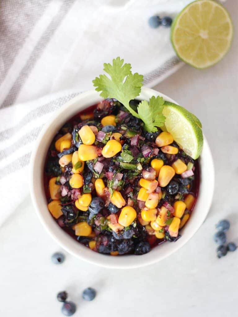 Blueberry and corn salsa in a white bowl garnished with a fresh lime slice and cilantro.