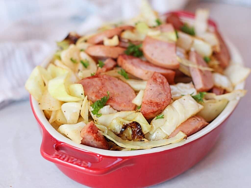 Browned sliced sausage and cabbage in a red serving bowl.