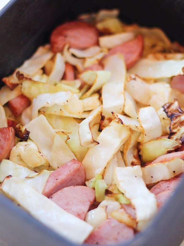 Kielbasa and cabbage in an air fryer basket.